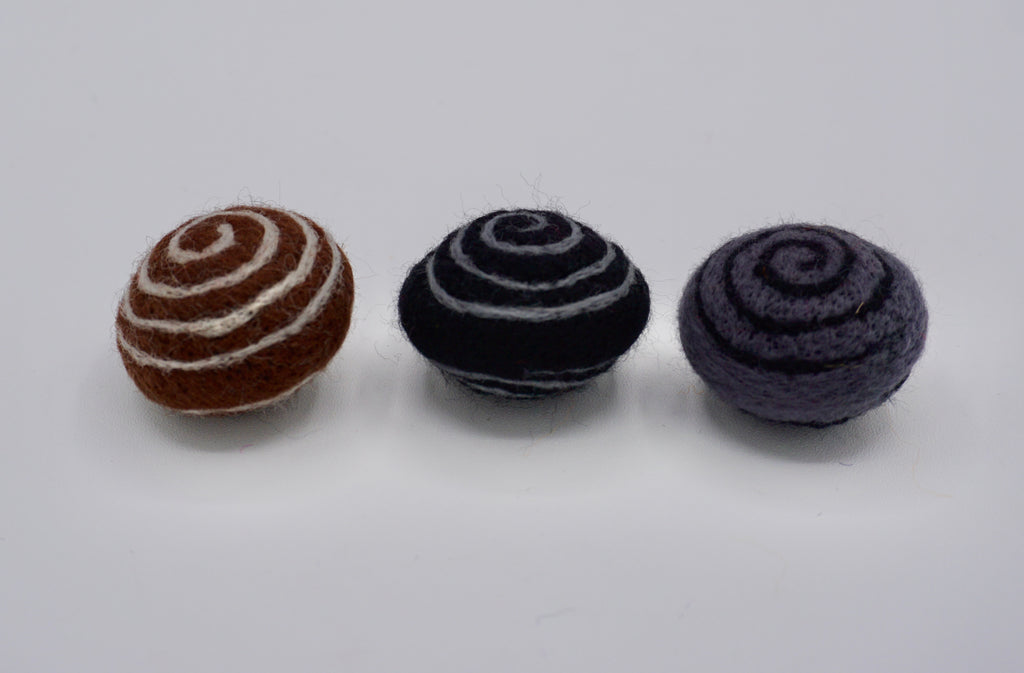 Three small swirly felt with spiral-shape toys in brown and white, black and gray, and brown & white. 